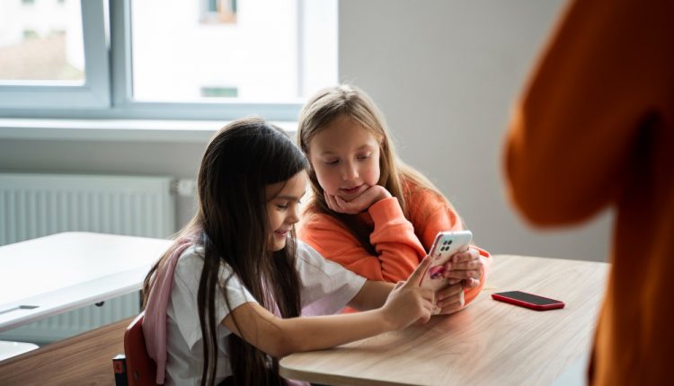 Duas meninas na sala de aula com o celular na mão