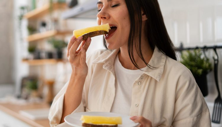 Mulher com cabelos soltos comendo fatia de queijo