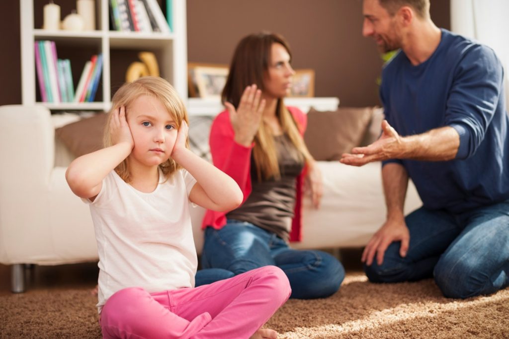 Homem e mulher discutindo num ambiente doméstico  e uma criança com as mãos nos ouvidos