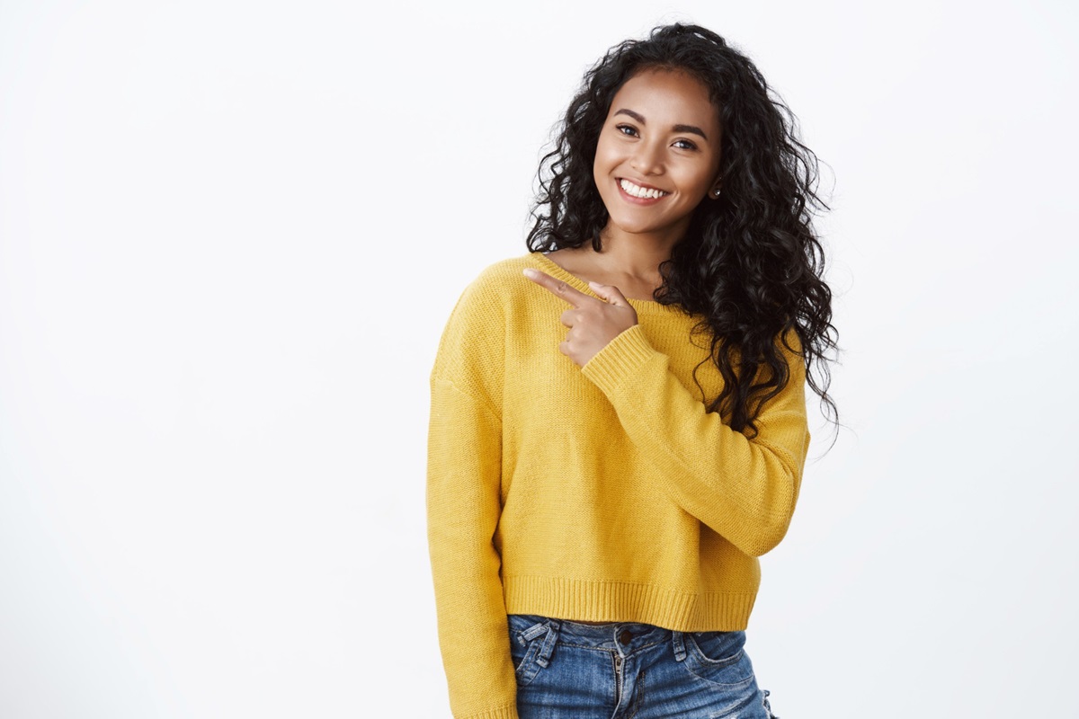 Mulher com blusa amarela e cabelos soltos com semblante feliz