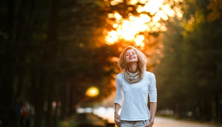 Mulher sorridente caminhando ao ar livre em um parque ao entardecer, expressando felicidade e bem-estar