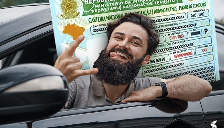 Homem sorridente dentro de um carro, fazendo um gesto de 'rock' com a mão e exibindo uma carteira de habilitação do Brasil em tamanho ampliado ao fundo