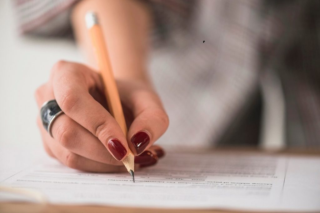 Candidata com unhas pintas e lápis na mão estudando para o processo seletivo da Prefeitura de Eldorado, no estado do Mato Grosso.