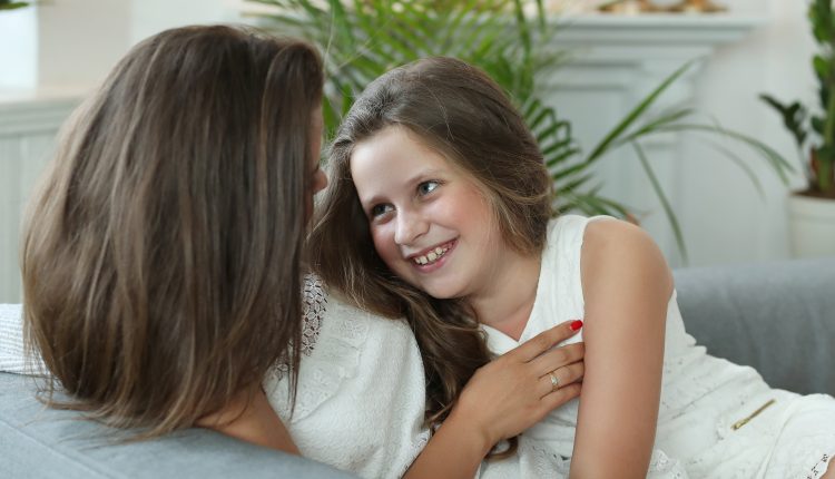 Filha sentada no colo e sorrindo para a mãe.