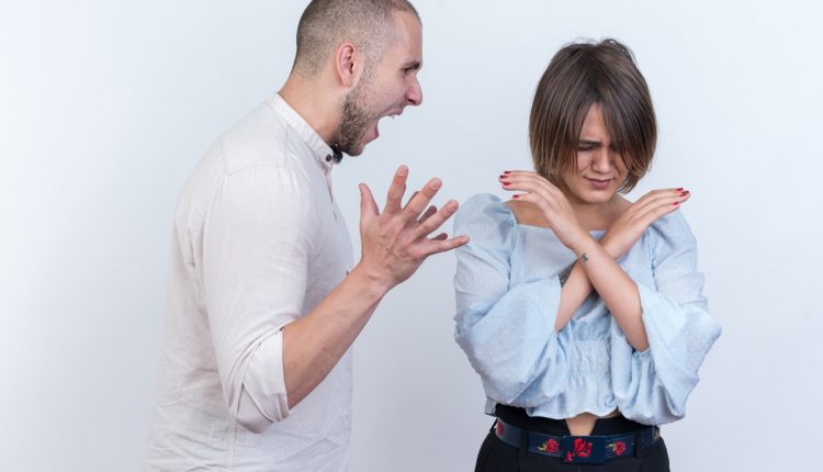 Homem gritando enquanto mulher se protege cruzando os braços, demonstrando desconforto em um conflito.