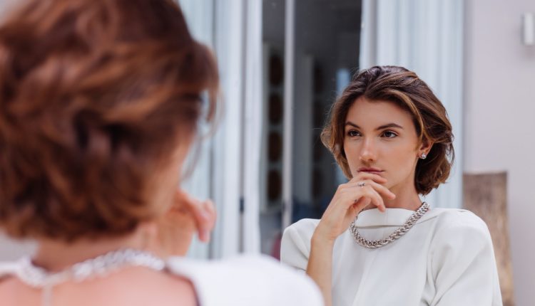 Mulher olhando para o espelho com expressão reflexiva, representando traços sombrios da personalidade.