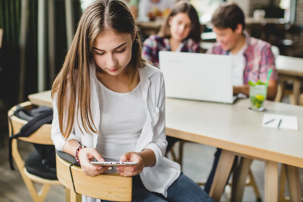 Jovem da Geração Z usando smartphone no trabalho, representando o relaxamento durante o expediente