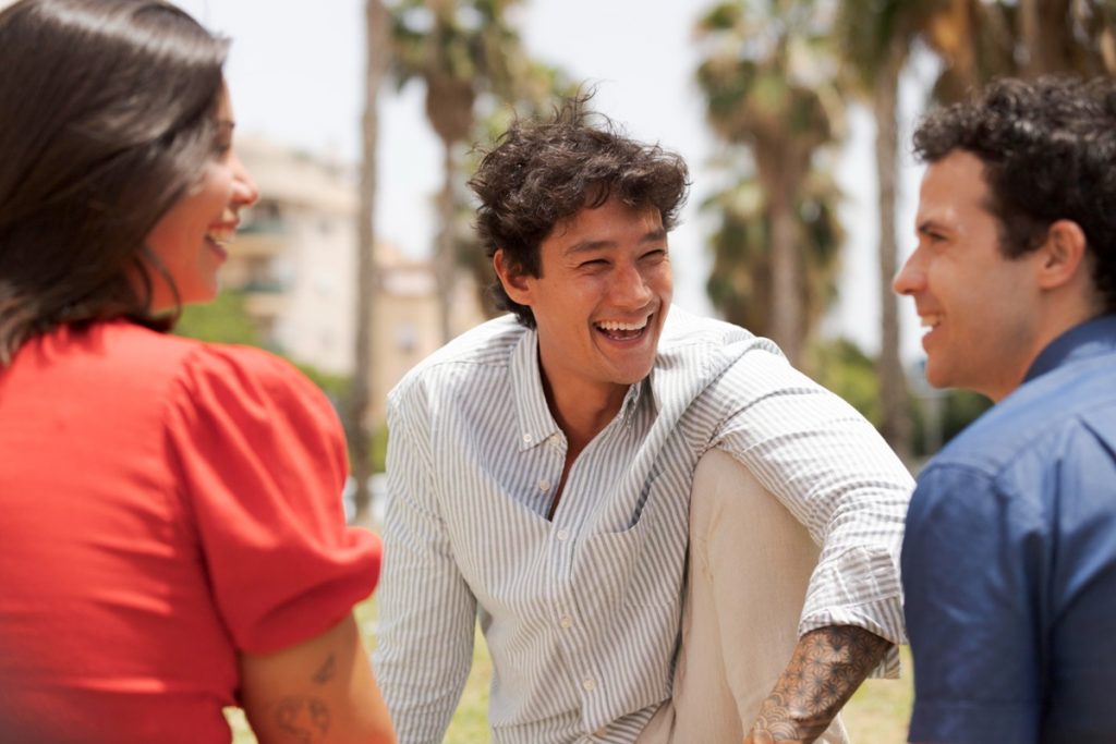 Grupo de amigos sorrindo e conversando ao ar livre em um dia ensolarado.