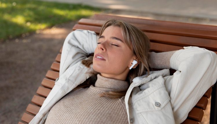 Mulher relaxando em um banco ao ar livre com fones de ouvido e olhos fechados