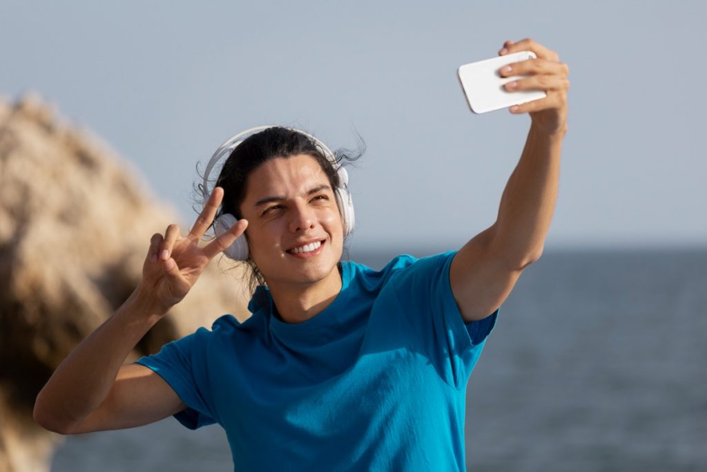 Jovem tirando selfie na praia, simbolizando autoestima e bem-estar