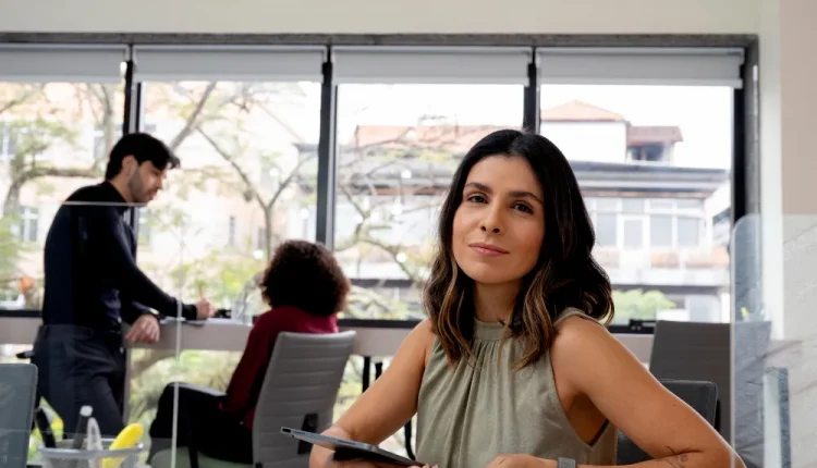 Mulher sorrindo em escritório moderno com ambiente colaborativo e profissionais ao fundo