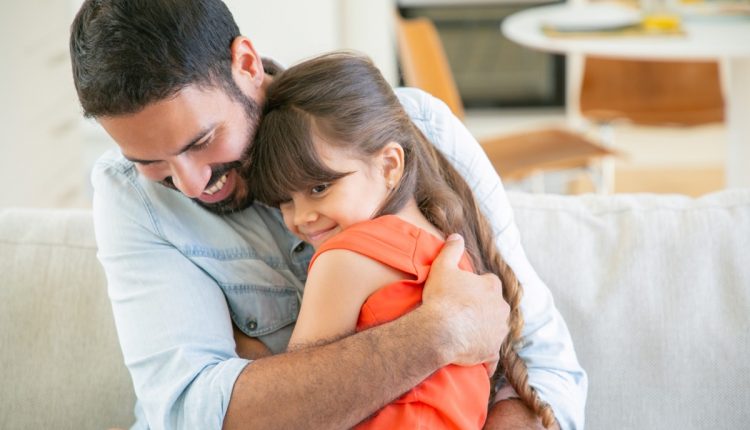 Pai abraçando carinhosamente sua filha no sofá, demonstrando conexão emocional.