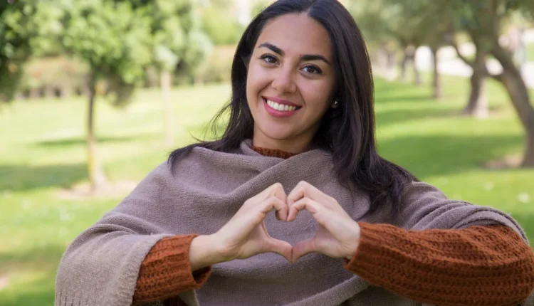 Mulher sorridente fazendo o gesto de coração com as mãos, simbolizando o autocuidado e a importância de aprender a dizer ‘não’.