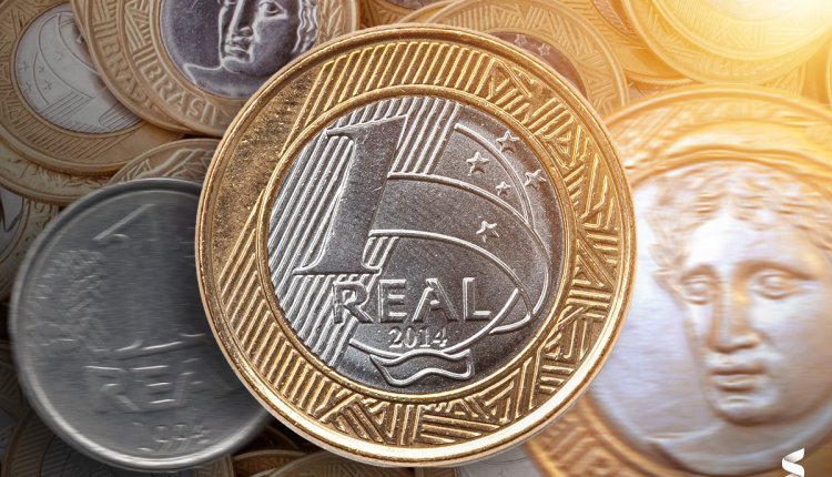 Imagem de moedas de 1 real, destacando a moeda de 1 real de 2014, com referência à moeda de 1 real de 1998 e seus erros de cunhagem, que podem aumentar seu valor até R$ 2.500.