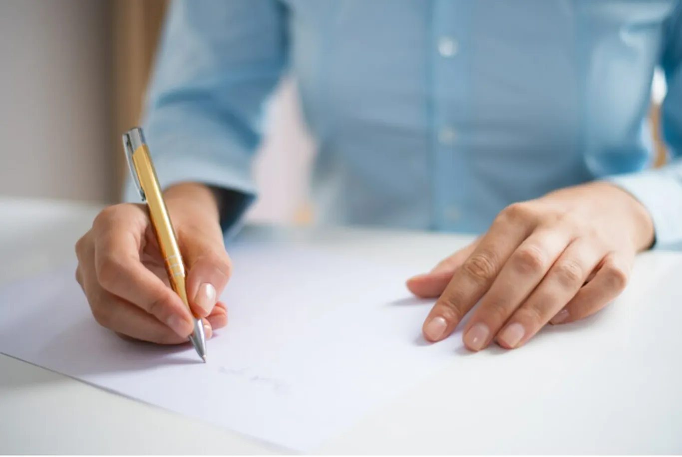 Mãos de uma pessoa escrevendo em uma folha de papel branco, representando a organização de documentos para um processo seletivo