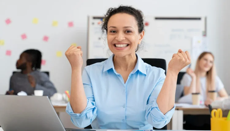 Mulher sorridente comemorando uma conquista no ambiente de trabalho, representando sucesso profissional.