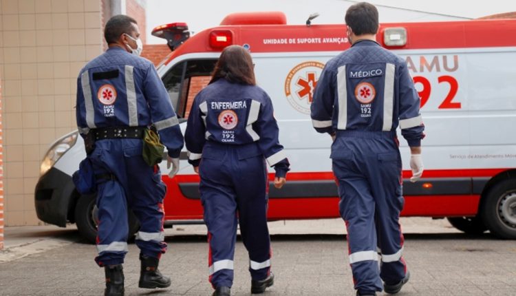 Profissionais do SAMU em uniforme, incluindo enfermeira, médico e técnico, em frente à ambulância do SAMU.