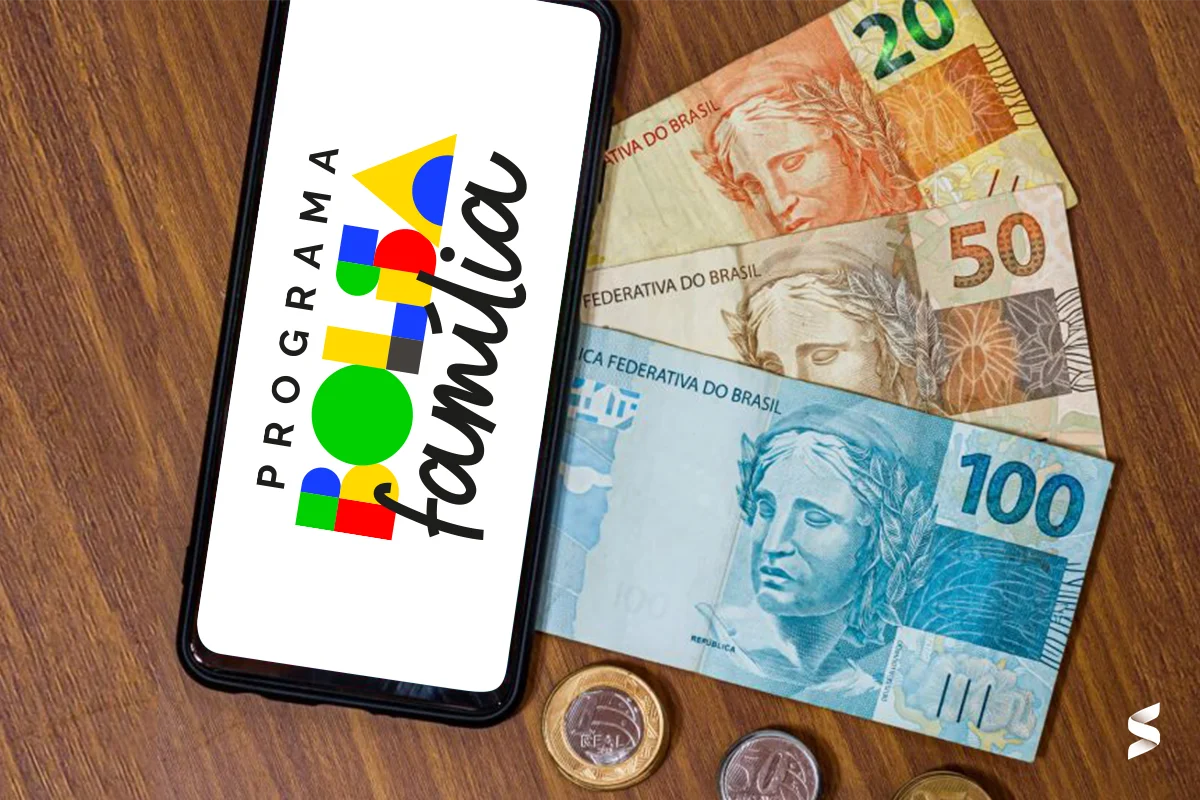 Tela de celular com logo do Programa Bolsa Família ao lado de notas de dinheiro