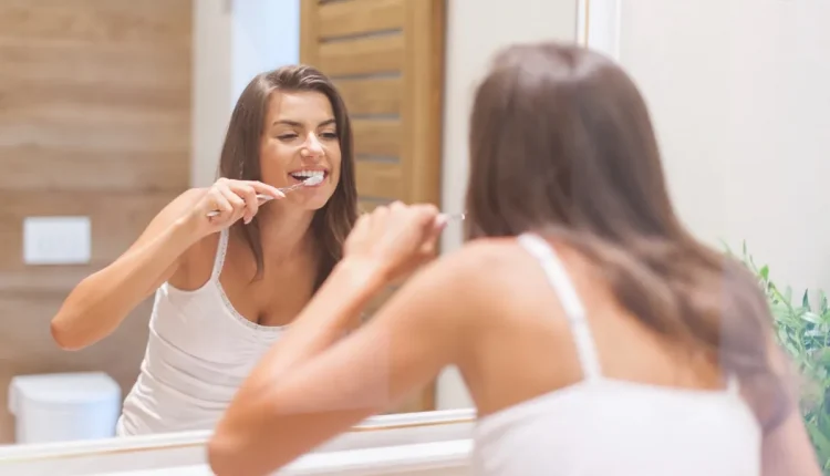 Mulher escovando os dentes em frente ao espelho do banheiro.