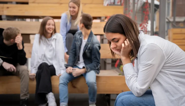 Pessoa isolada em um grupo de amigos, representando a dificuldade de socializar na vida adulta.