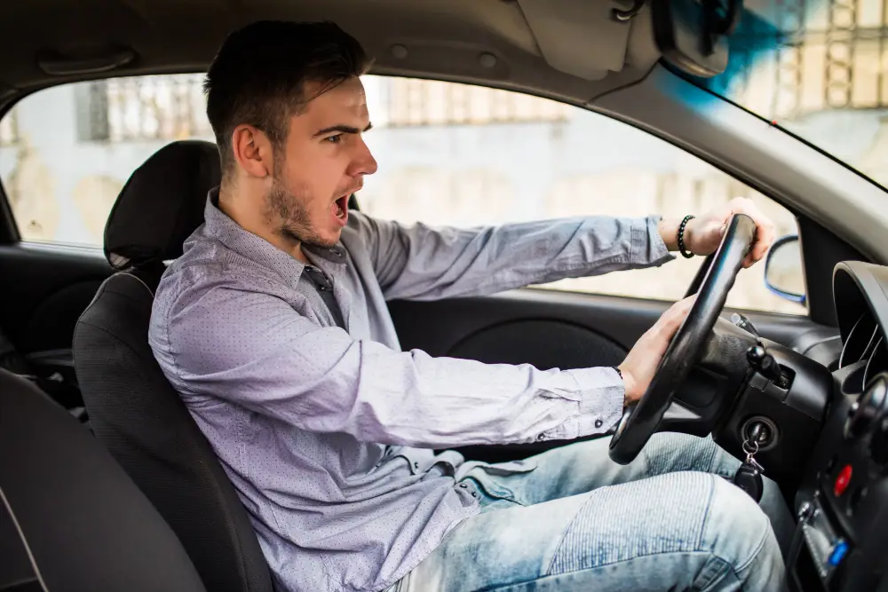 Motorista demonstrando raiva ao volante, ilustrando como emoções negativas podem afetar a segurança no trânsito.