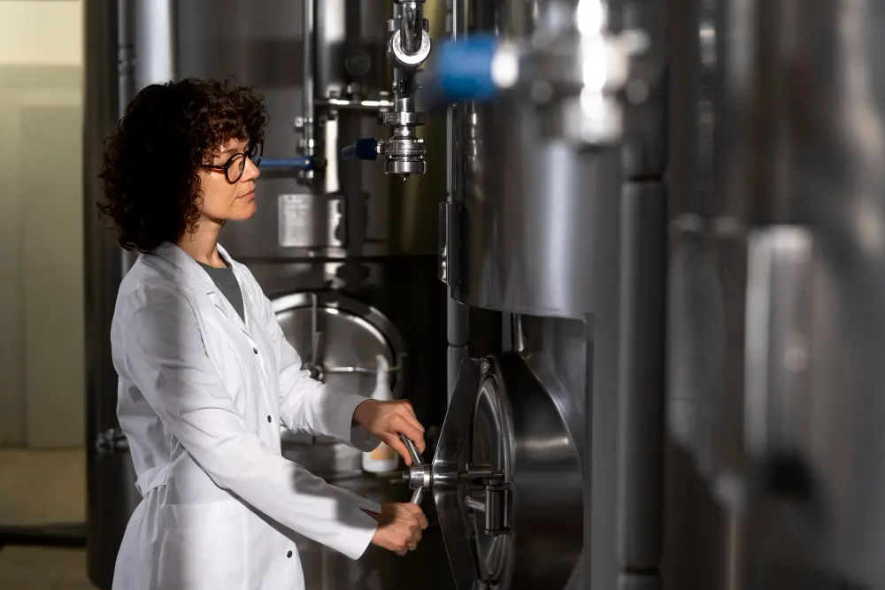 Mulher em um laboratório de engenharia química, utilizando equipamentos industriais para monitoramento e controle de processos.