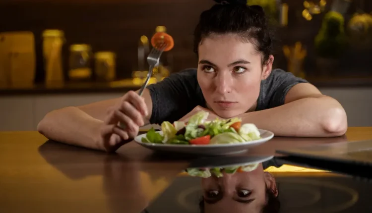 Mulher olhando fixamente para um prato de salada com expressão séria.