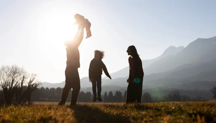 Família brincando ao ar livre ao pôr do sol, com pai levantando uma criança no ar.