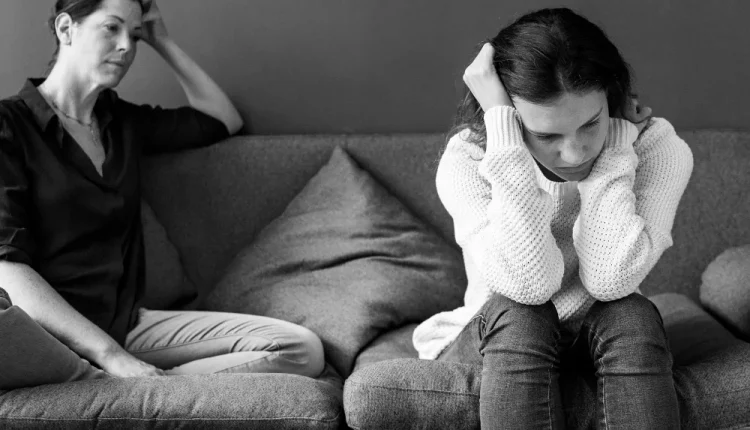 Mãe e filha sentadas no sofá, distantes emocionalmente, representando a falta de empatia na comunicação.