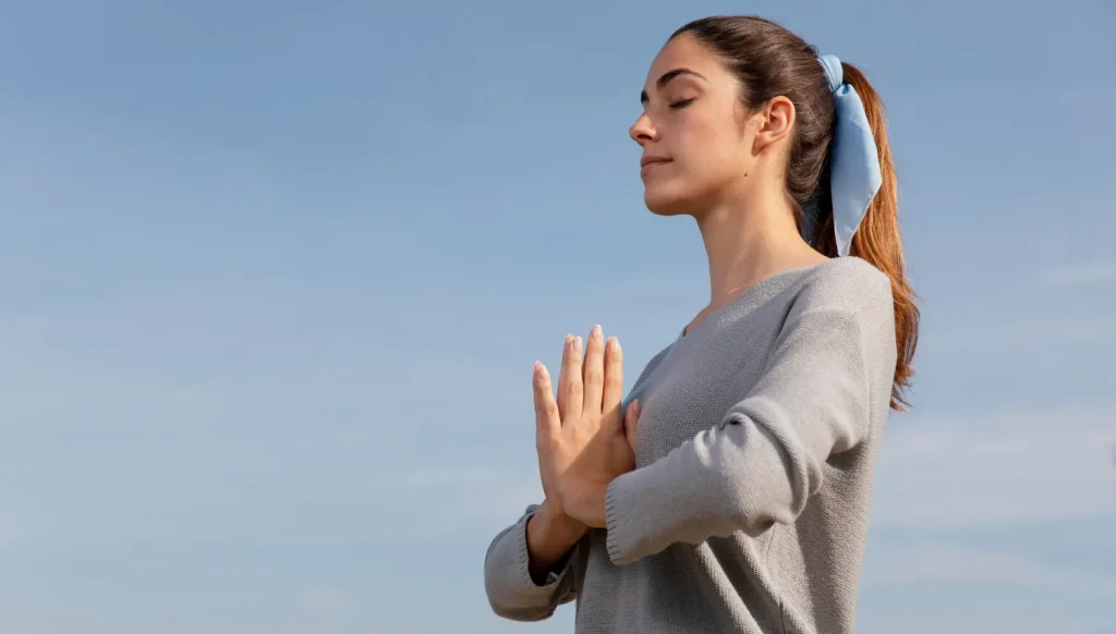 Mulher jovem meditando ao ar livre com as mãos em posição de prece, transmitindo paz e positividade