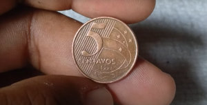 Moeda de 5 centavos de 1999 segurada por uma mão, podendo valer até R$200 no mercado de colecionadores.