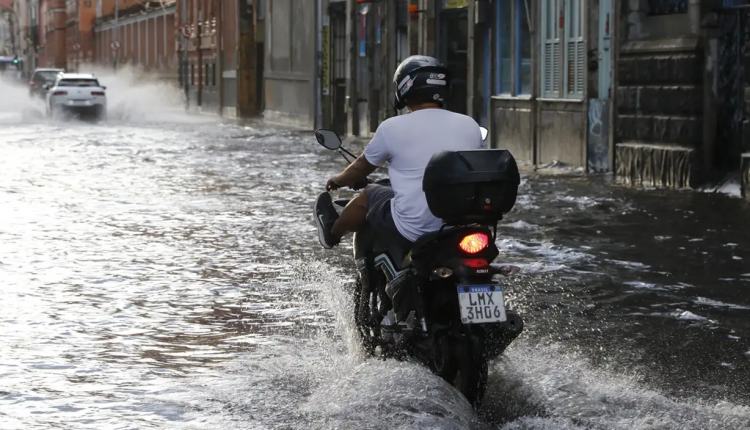 Motociclista atravessa rua alagada após forte chuva em área urbana.