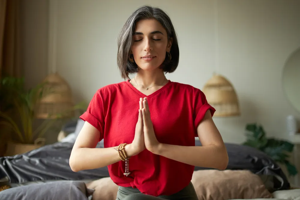 Mulher em meditação com as mãos unidas, praticando mindfulness e autorreflexão.