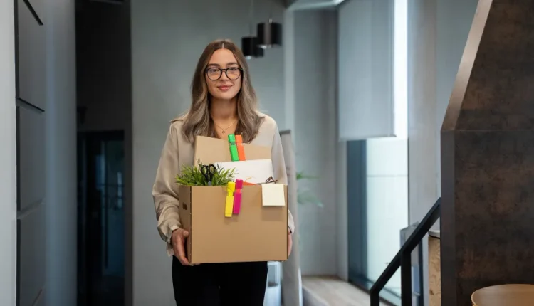 Mulher saindo do trabalho com uma caixa de papelão, simbolizando a mudança de emprego.