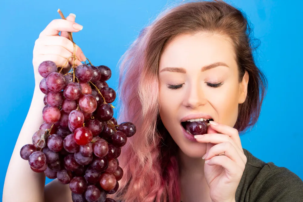 Mulher segurando um cacho de uvas e consumindo uma, destacando sua importância na nutrição esportiva.