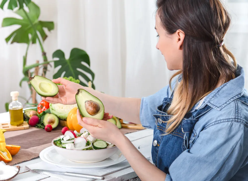 Mulher preparando uma salada fresca com abacate, um alimento rico em gorduras saudáveis.