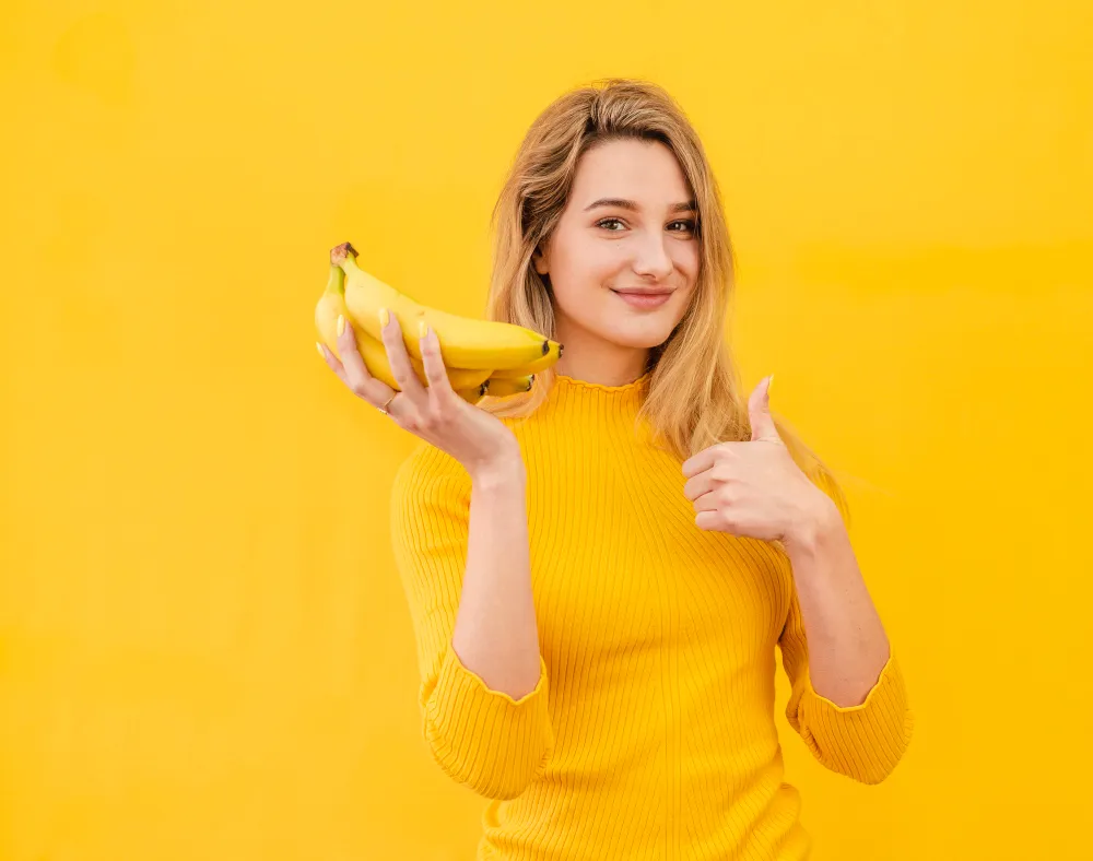 Mulher sorrindo e segurando bananas, representando alimentação saudável e energia para treinos