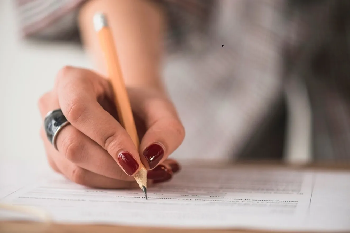 Mão feminina preenchendo um formulário com lápis, representando preparação para concurso público.