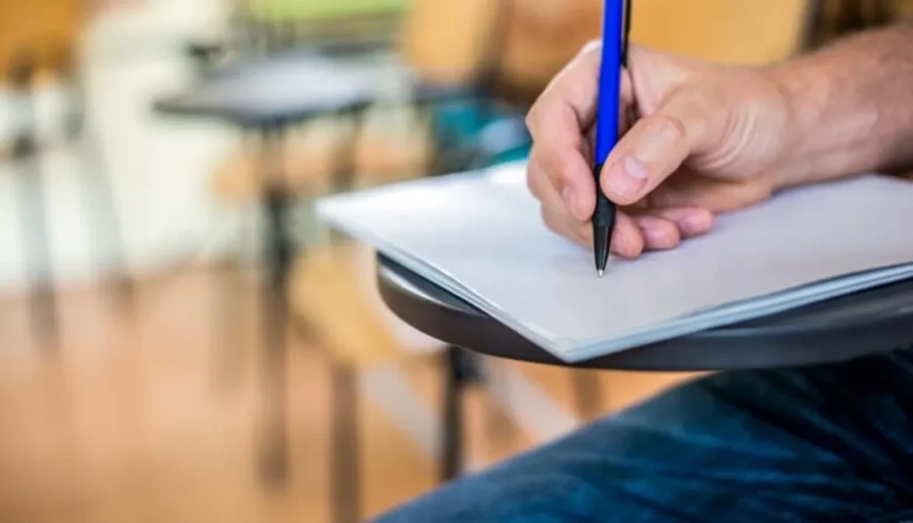 Mão segurando uma caneta, pronta para escrever em uma folha de papel em um ambiente de estudo