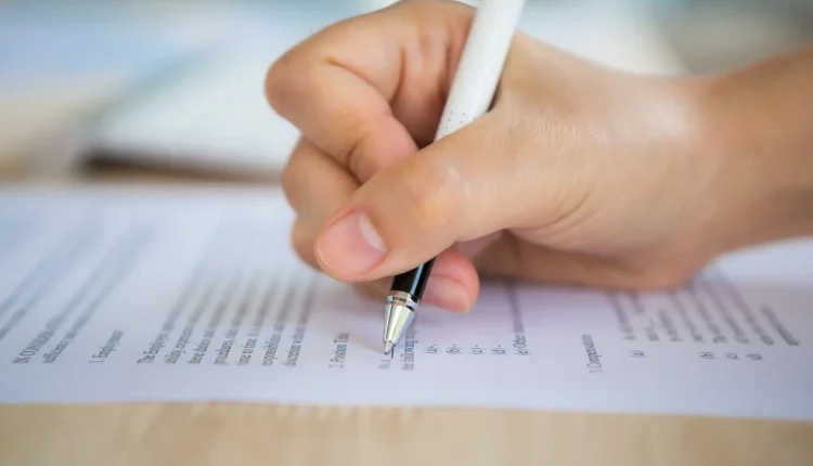 Mão preenchendo um formulário de prova, representando um processo seletivo