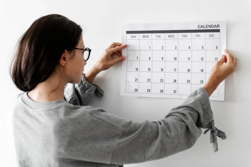 Mulher fixando um calendário na parede, representando o papel da repetição na construção de hábitos