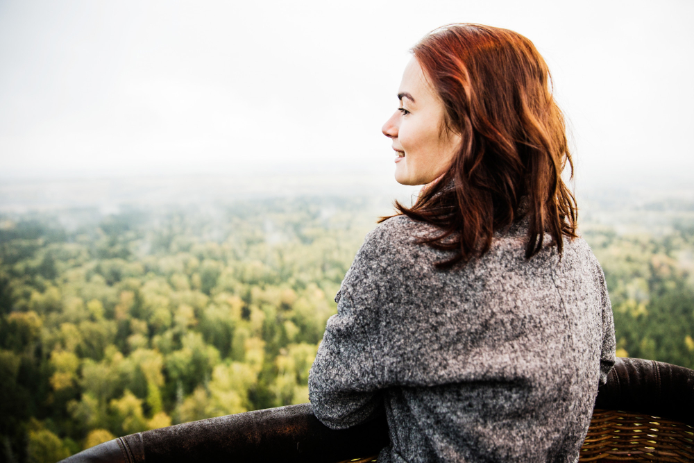 Mulher admirando a paisagem de uma floresta do alto, em um momento de contemplação.