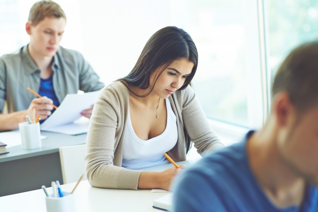 Imagem de estudantes realizando uma prova ou exercício, representando as etapas de seleção de um concurso público.