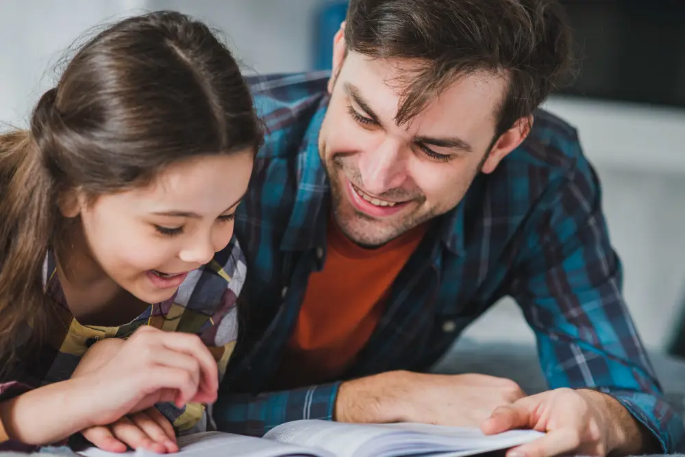 Pai e filha sorrindo enquanto leem juntos, simbolizando a conexão e o aprendizado compartilhado.