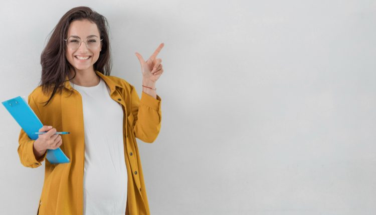 Mulher sorridente segurando um bloco de anotações e apontando para cima, representando sucesso na carreira.