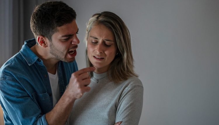 Homem agressivo discutindo com uma mulher que aparenta estar desconfortável, simbolizando um relacionamento abusivo.