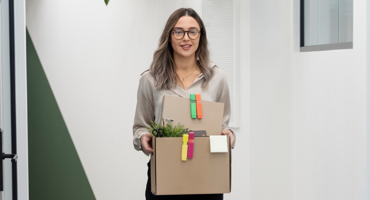 Mulher segurando uma caixa com objetos de escritório, simbolizando a adaptabilidade a mudanças no ambiente de trabalho.