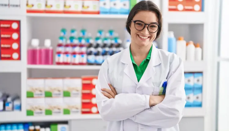 Farmacêutica sorrindo com os braços cruzados em uma farmácia, transmitindo confiança e competência.