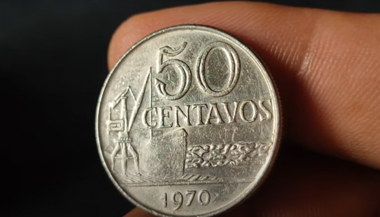 Moeda de 50 centavos de 1970 sendo segurada por uma mão, destacando seus detalhes.