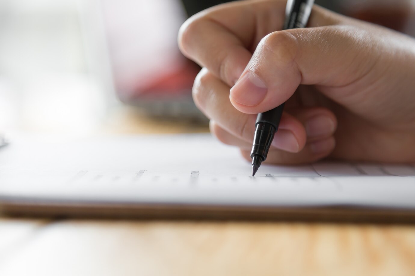 Mão segurando caneta e preenchendo uma ficha de inscrição para um processo seletivo.